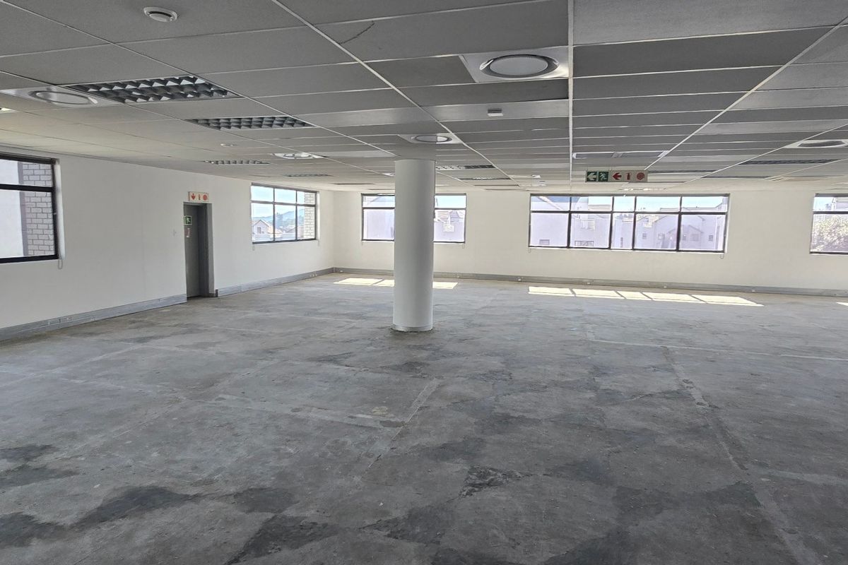 A spacious, open-plan commercial office area featuring a suspended ceiling, recessed lighting, and large windows, currently awaiting floor finishes and final fit-out.