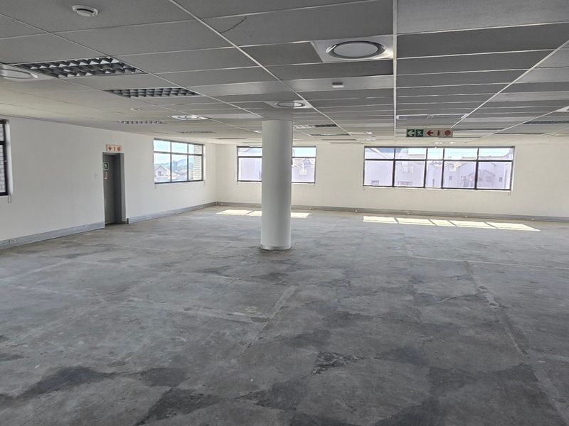A spacious, open-plan commercial office area featuring a suspended ceiling, recessed lighting, and large windows, currently awaiting floor finishes and final fit-out.