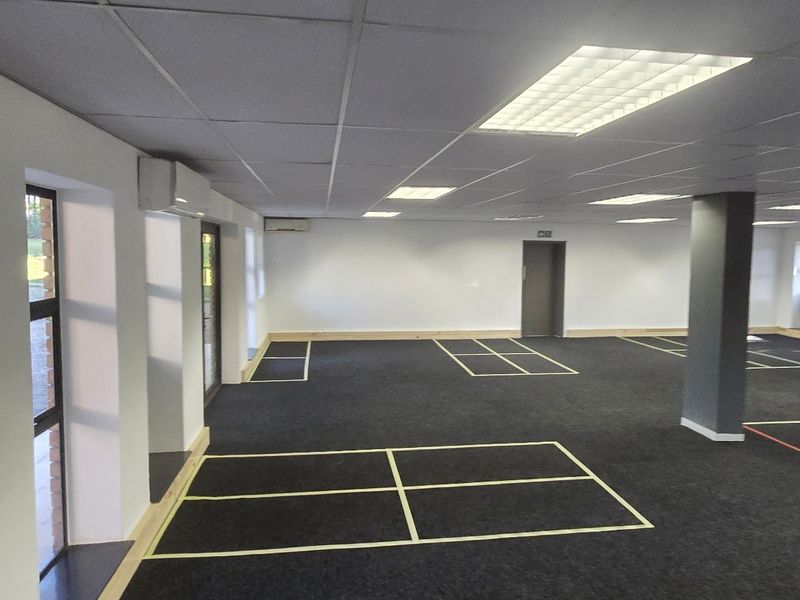 Spacious open-plan commercial office area featuring a suspended ceiling, recessed lighting, air conditioning, and large windows providing ample natural light.