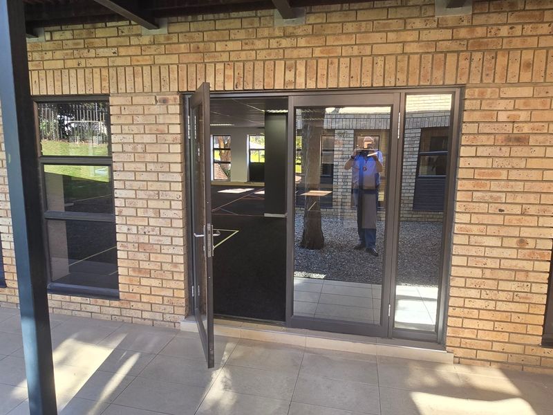 A covered patio area featuring face brick walls, tiled flooring, and aluminium framed glass doors providing access to the interior office space.