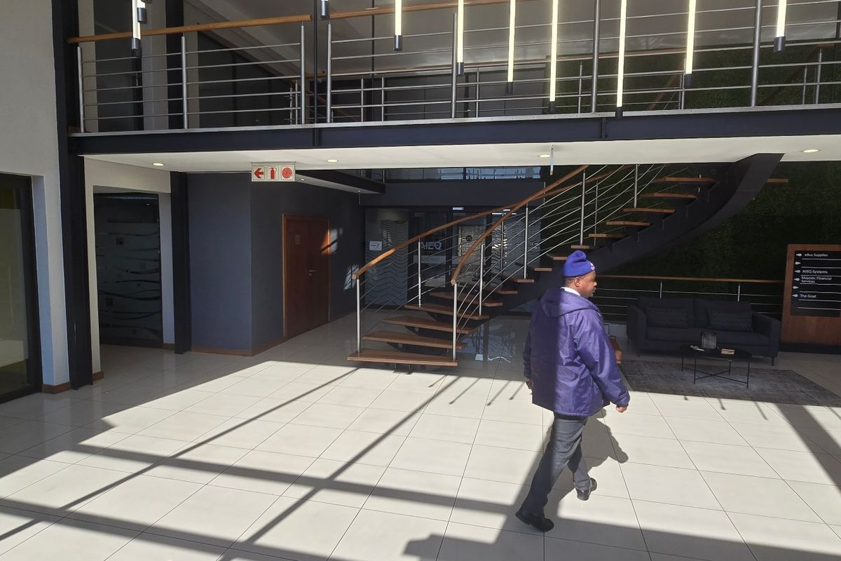 Modern commercial building entrance featuring a double-volume lobby, a striking wooden staircase with stainless steel balustrades, and a feature vertical garden wall.
