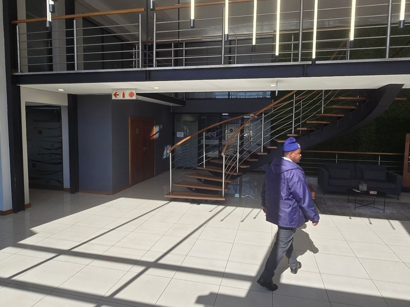 Modern commercial building entrance featuring a double-volume lobby, a striking wooden staircase with stainless steel balustrades, and a feature vertical garden wall.