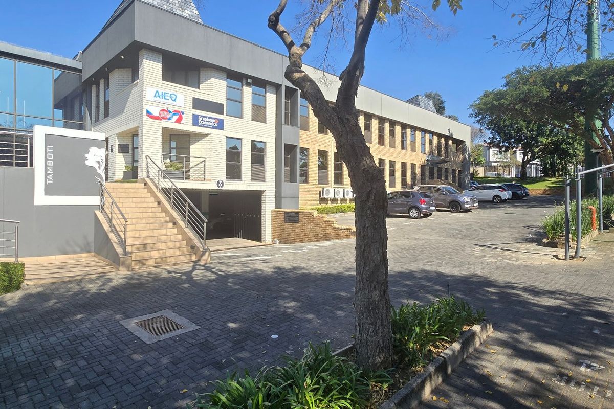 Front exterior view of a modern commercial office building featuring a paved parking area, brick and glass facade, and external staircase access.