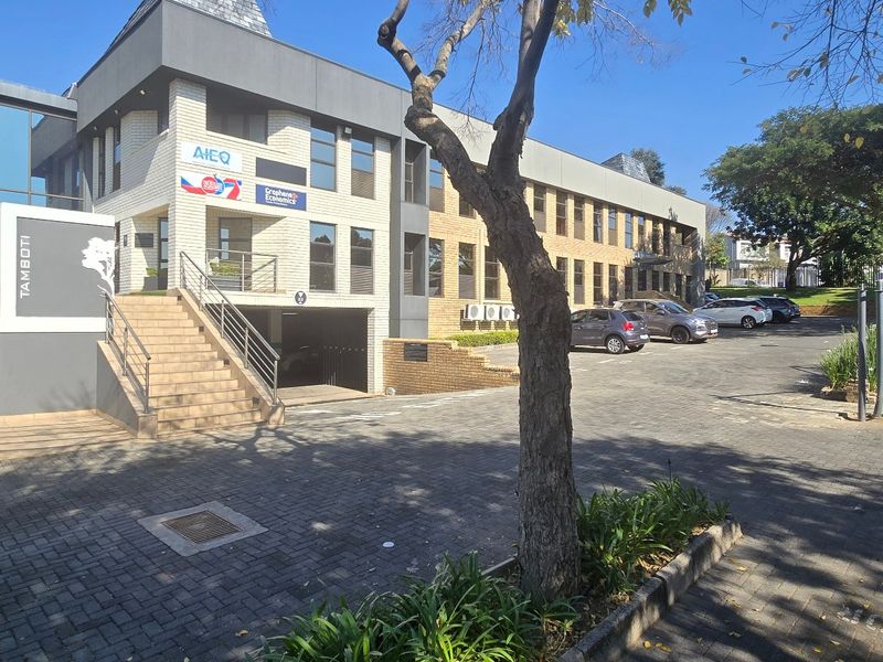 Front exterior view of a modern commercial office building featuring a paved parking area, brick and glass facade, and external staircase access.