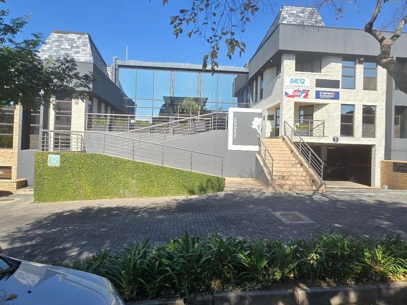 Modern commercial office building exterior featuring a paved driveway, ramp access, glass facade, and professional brick finish.