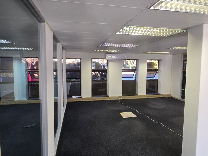 An open-plan commercial office space featuring carpet tiles, suspended ceilings with recessed lighting, air conditioning, and glass partitioning.