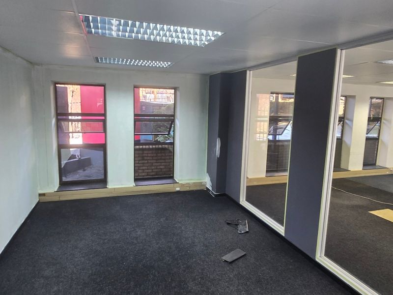 An empty commercial office space featuring glass partitions, carpeted flooring, recessed lighting, and an integrated air conditioning unit.