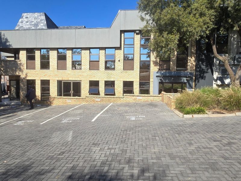 Front exterior view of a commercial office building featuring a brick facade, multi-pane windows, and a paved visitor parking area.