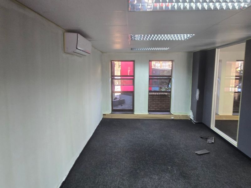 An empty commercial office space featuring carpet flooring, recessed lighting, a split-system air conditioner, and glass partition walls.