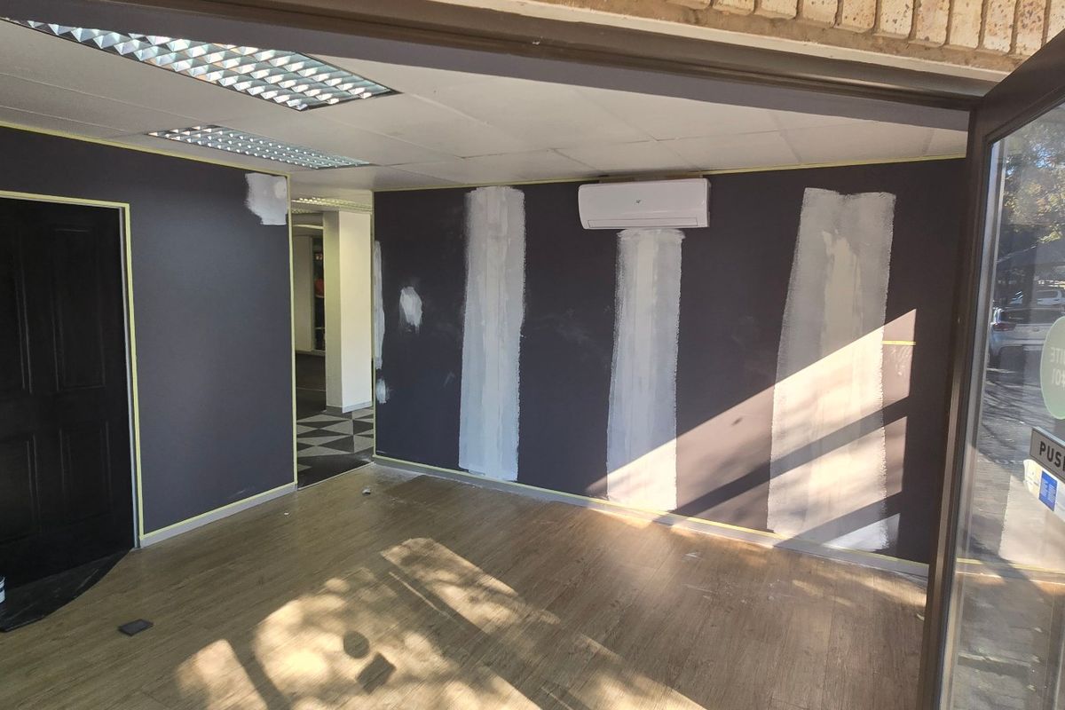 An empty commercial office space currently undergoing renovations, featuring laminate flooring, a split-system air conditioner, and unfinished wall surfaces.