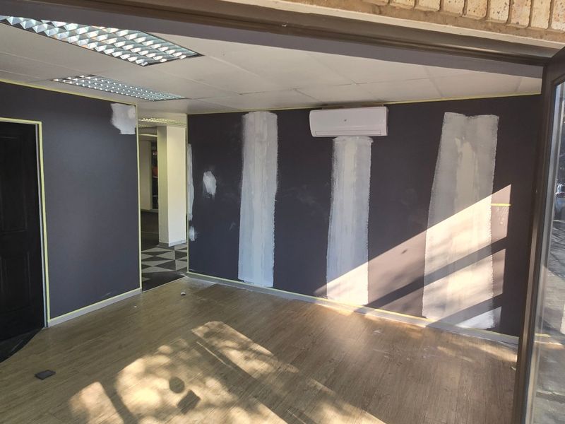 An empty commercial office space currently undergoing renovations, featuring laminate flooring, a split-system air conditioner, and unfinished wall surfaces.