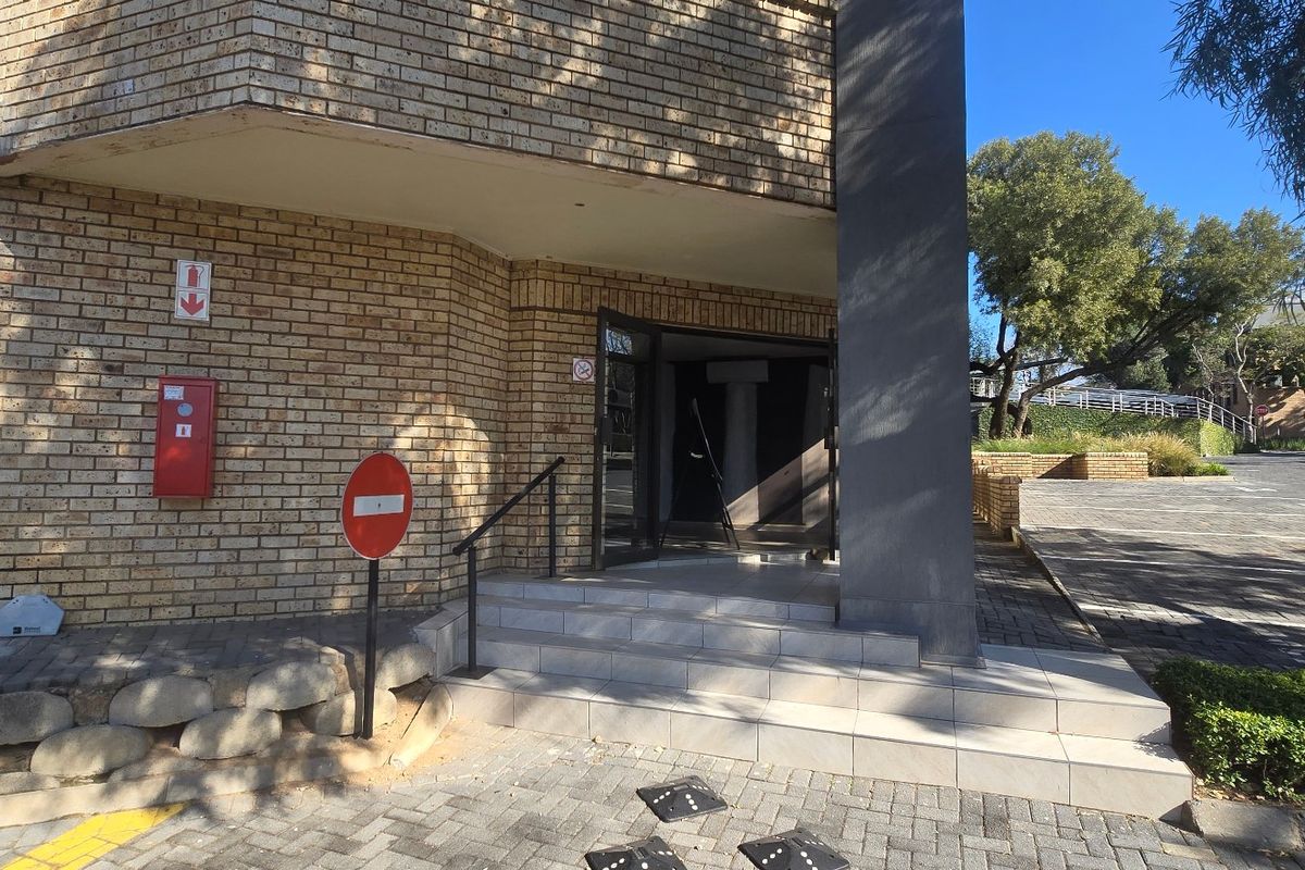 Commercial building entrance featuring a brick facade, tiled steps with a metal handrail, and a paved driveway approach.
