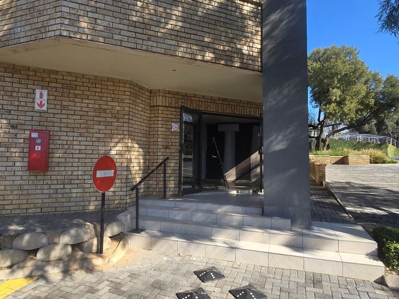 Commercial building entrance featuring a brick facade, tiled steps with a metal handrail, and a paved driveway approach.