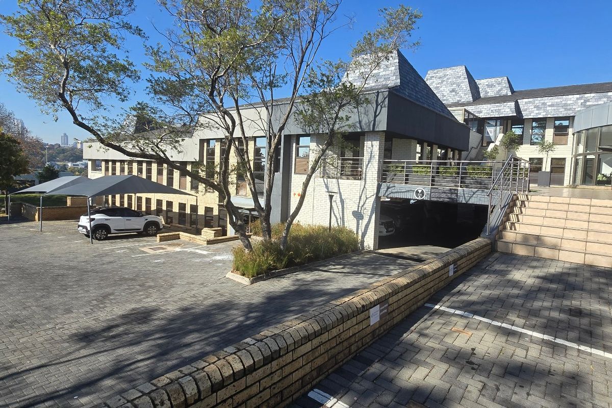Exterior view of a commercial property featuring a paved driveway, covered parking, and a multi-level building facade with slate roofing.