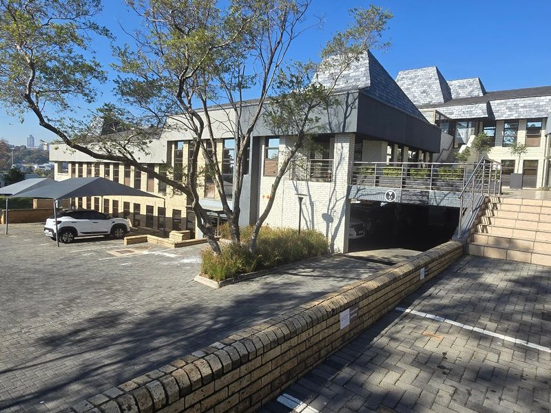 Exterior view of a commercial property featuring a paved driveway, covered parking, and a multi-level building facade with slate roofing.