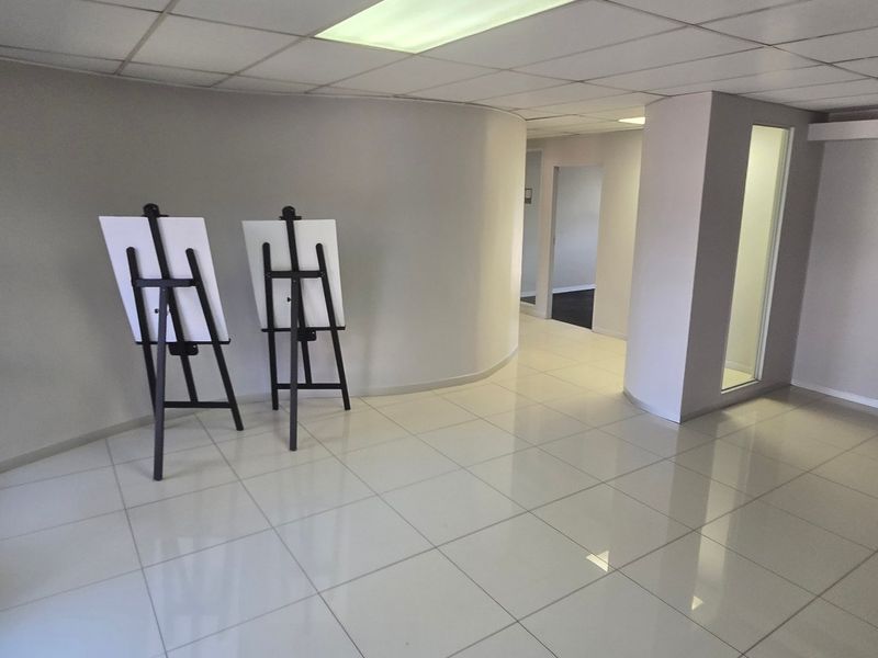 A bright, open-plan commercial office space featuring polished tiled flooring, a curved wall design, and a suspended ceiling with recessed lighting.