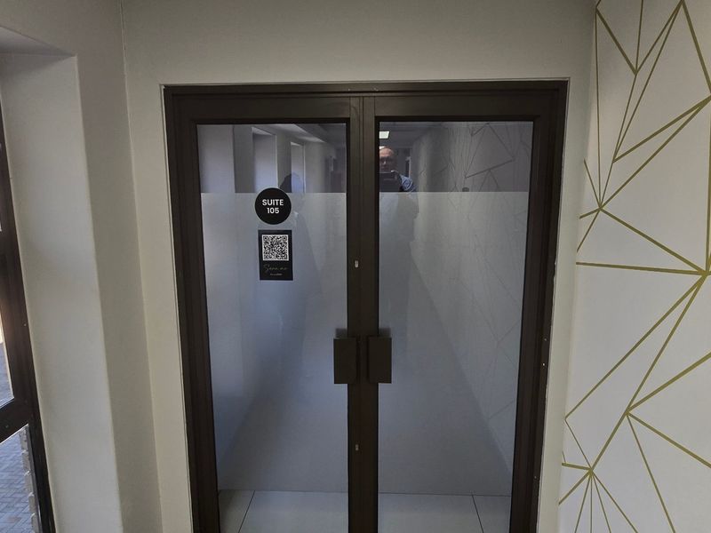 A modern commercial office entry featuring double glass doors with frosted privacy film, geometric wall detailing, and natural light from an adjacent window.