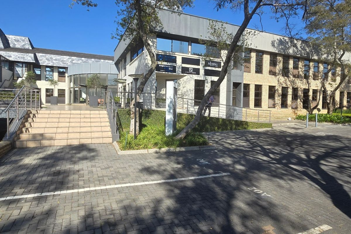Front exterior view of a multi-story commercial office building featuring brick cladding, paved parking, and a prominent central entrance staircase.
