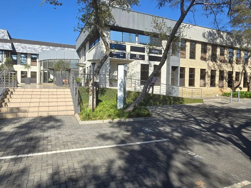 Front exterior view of a multi-story commercial office building featuring brick cladding, paved parking, and a prominent central entrance staircase.