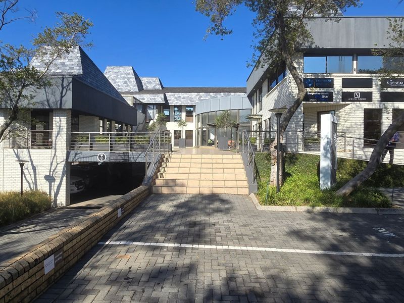 Front exterior view of a commercial office complex featuring brick facades, slate roofing, paved parking, and a central staircase leading to the main entrance.