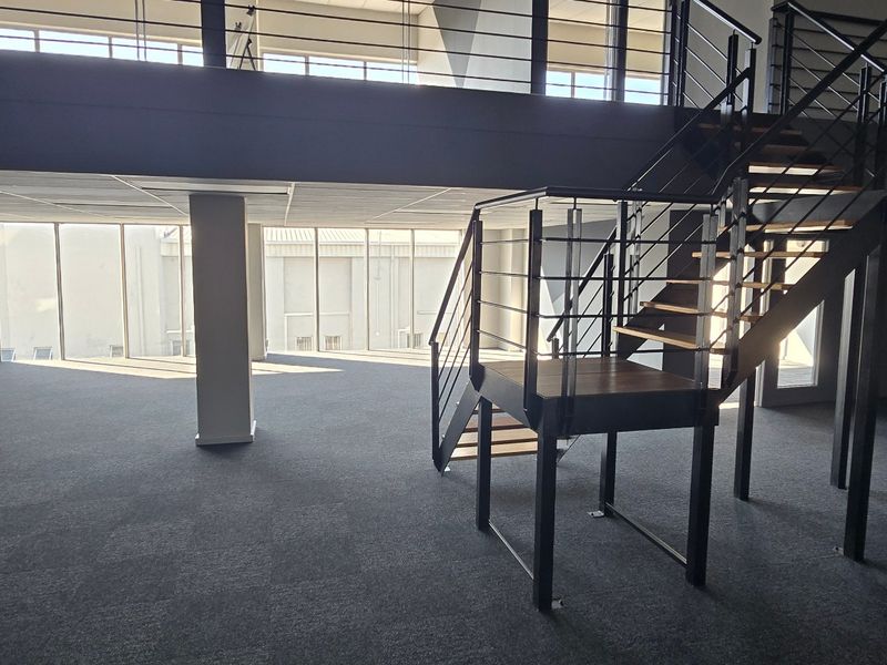 Spacious open-plan commercial office area featuring a modern mezzanine level, metal staircase, large windows for natural light, and split-system air conditioning.