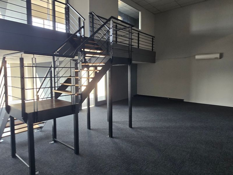 Spacious open-plan commercial office area featuring a modern metal staircase leading to a mezzanine level, carpeted flooring, and integrated air conditioning.