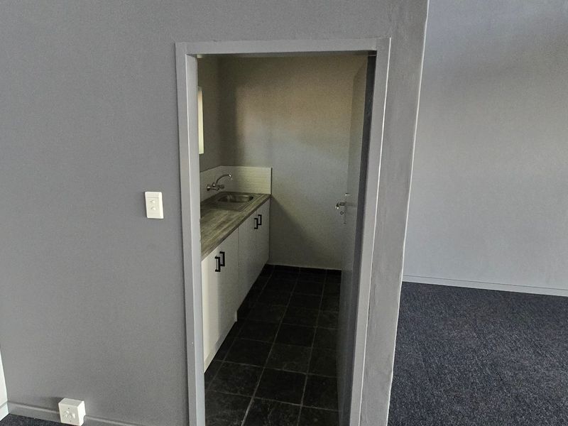 A compact, functional scullery or kitchenette area featuring built-in cabinetry, a sink, and durable tiled flooring, accessible from the main office space.