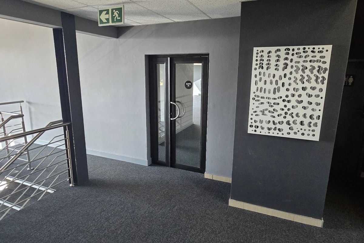 A modern commercial hallway featuring grey carpeting, a glass-panelled entrance door, and a stainless steel staircase railing.