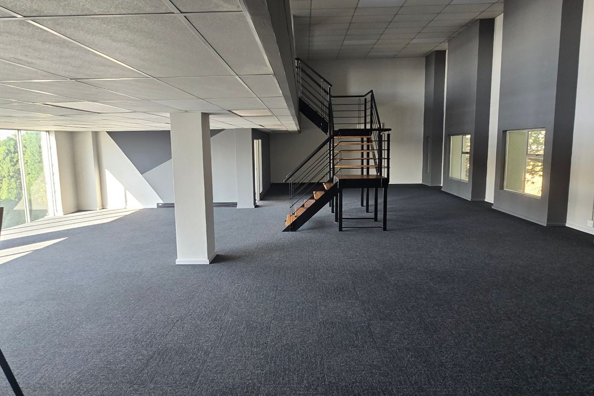 Spacious open-plan commercial office area featuring a modern metal staircase, suspended ceilings, and large windows providing ample natural light.