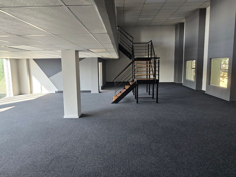 Spacious open-plan commercial office area featuring a modern metal staircase, suspended ceilings, and large windows providing ample natural light.