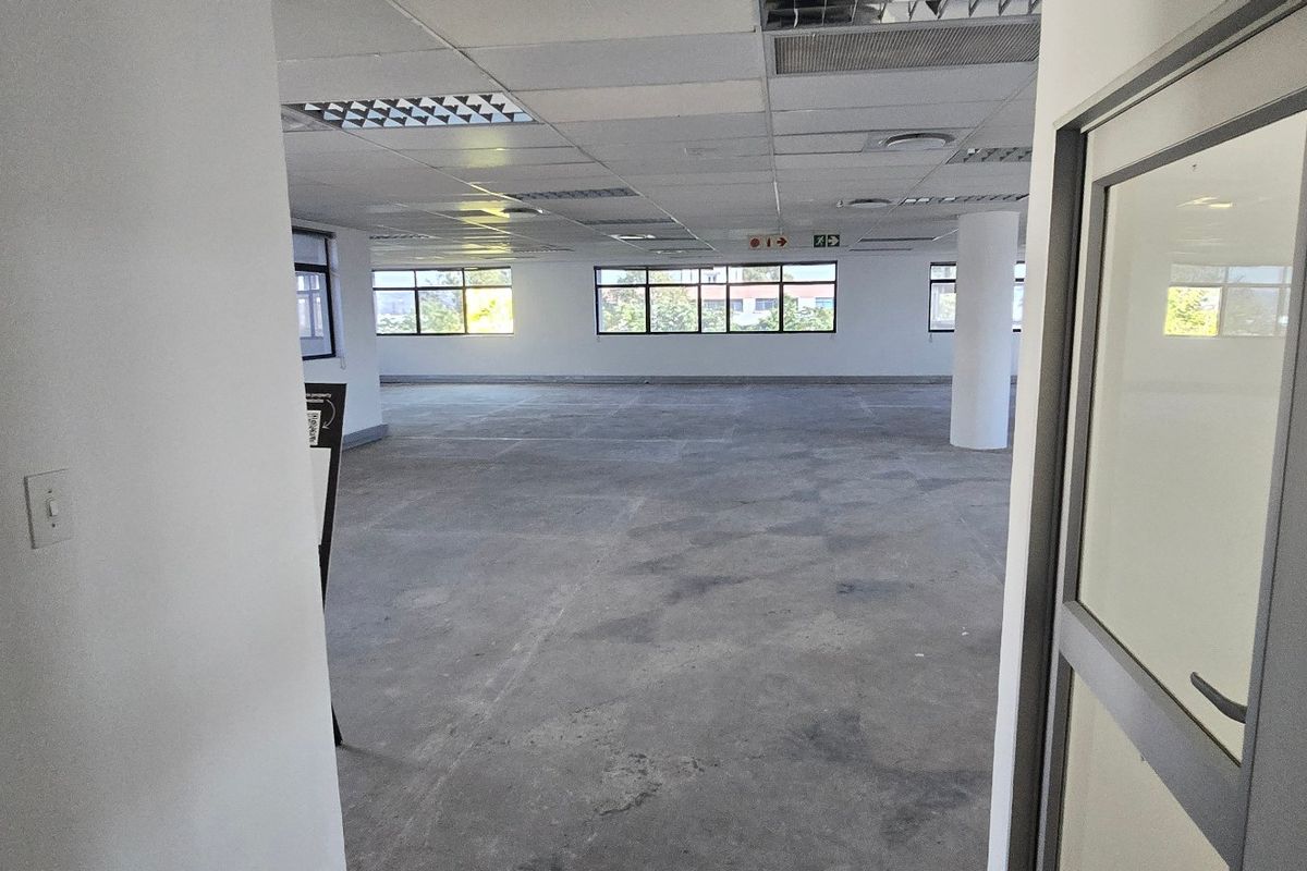 An open-plan commercial office space featuring a suspended ceiling, concrete flooring, and large windows providing natural light.