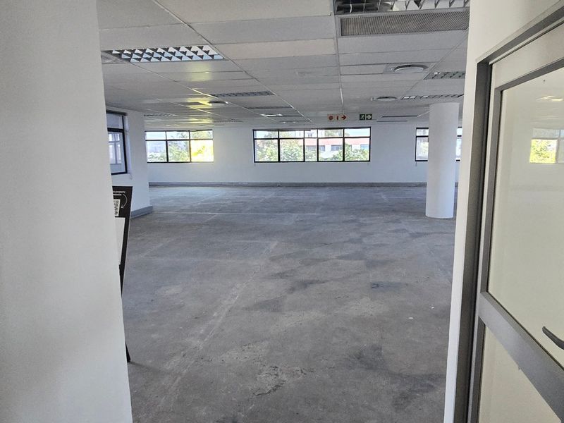 An open-plan commercial office space featuring a suspended ceiling, concrete flooring, and large windows providing natural light.