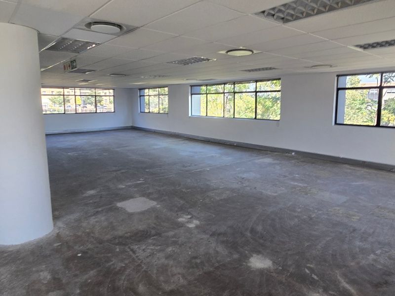 An open-plan commercial office space featuring a suspended ceiling, recessed lighting, and large windows, currently awaiting final floor finishes.