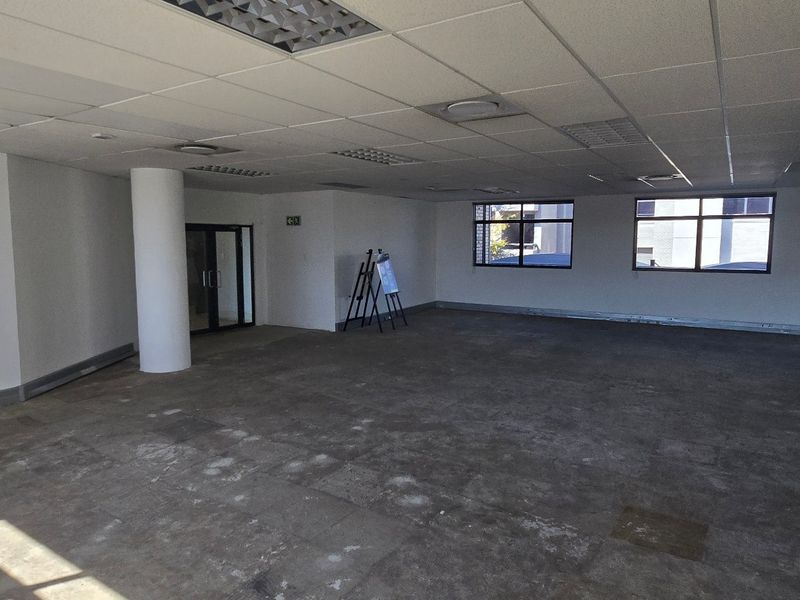 Open-plan commercial office space featuring structural columns, suspended ceilings with recessed lighting, and large windows providing natural light.