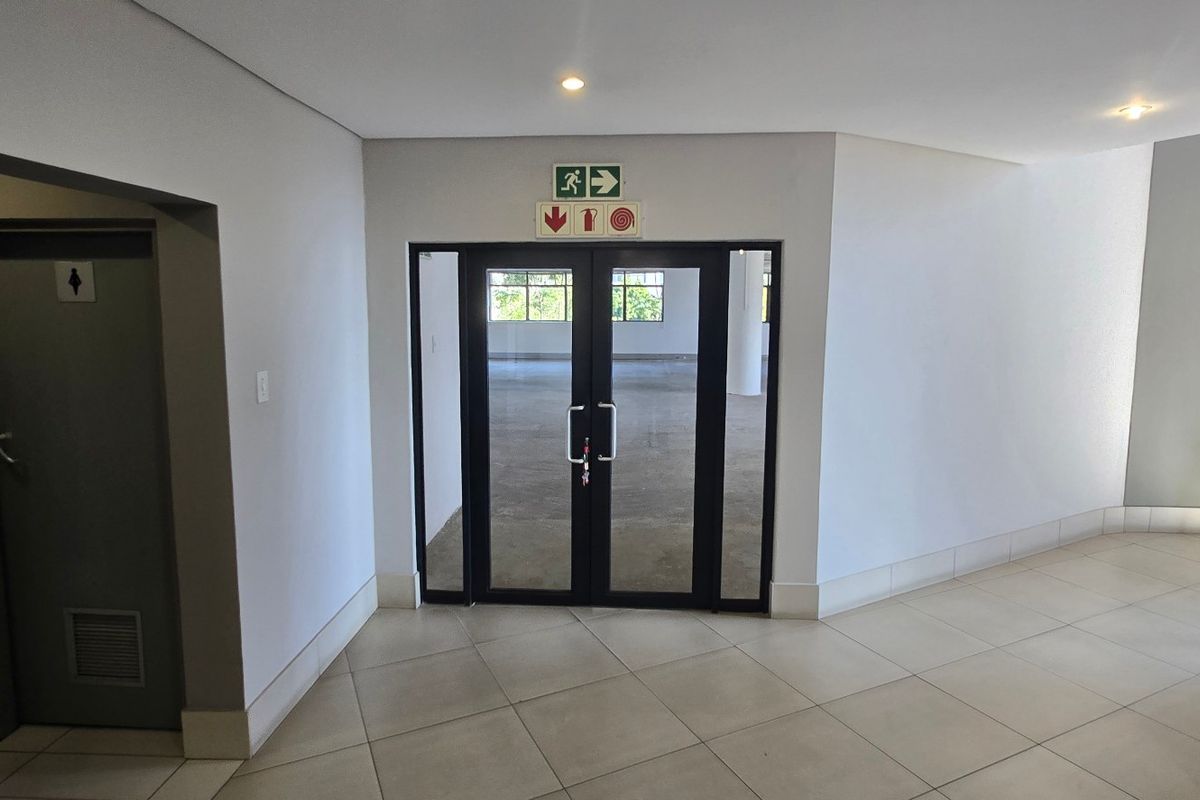 A clean, modern commercial entrance lobby featuring tiled flooring, recessed lighting, and double glass doors leading into an open-plan office space.