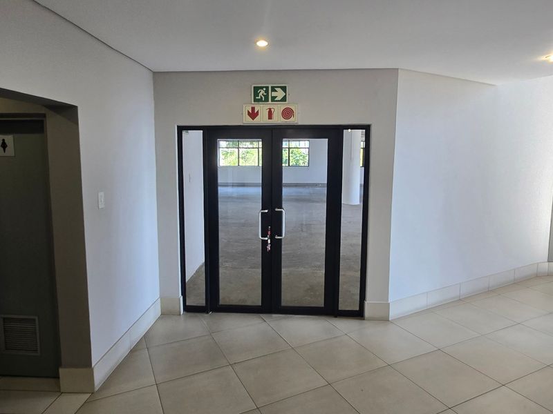 A clean, modern commercial entrance lobby featuring tiled flooring, recessed lighting, and double glass doors leading into an open-plan office space.