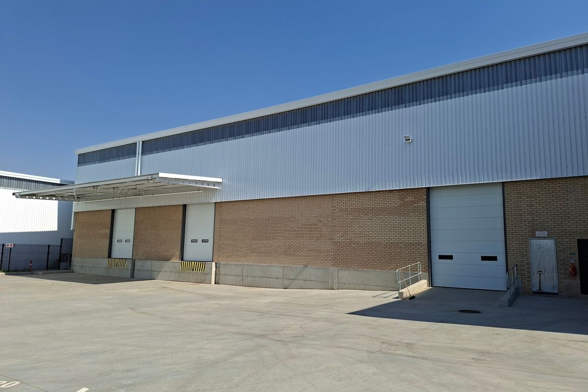 Industrial warehouse exterior featuring multiple roller shutter loading doors, a concrete loading apron, and a protective canopy over the loading bay area.