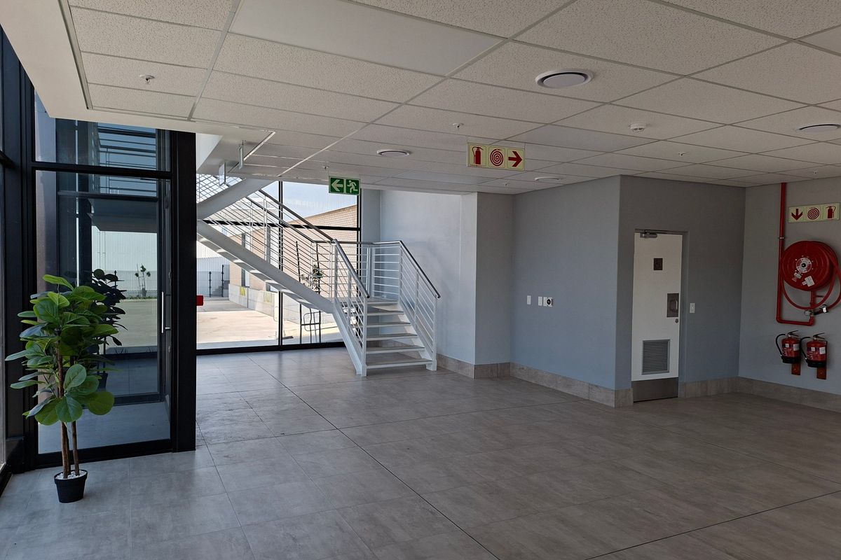 Modern industrial entrance lobby featuring tiled flooring, a clean suspended ceiling, a metal staircase, and integrated fire safety equipment.
