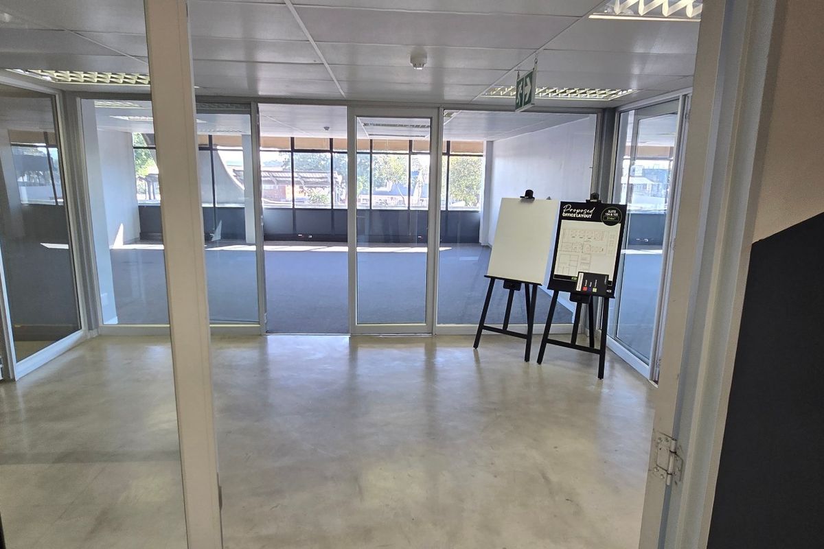 An open-plan commercial office space featuring glass partitions, suspended ceilings, and a mix of concrete and carpet flooring, offering a bright, professional workspace.