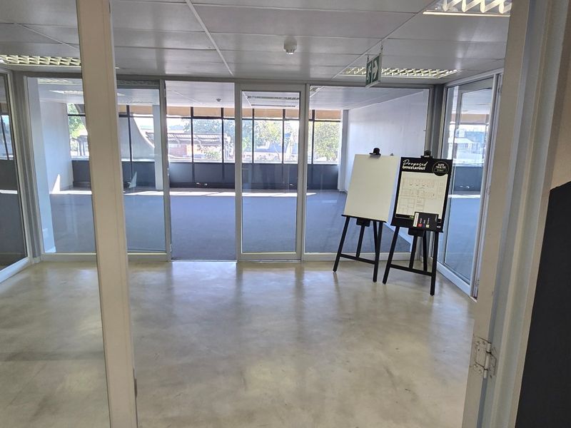 An open-plan commercial office space featuring glass partitions, suspended ceilings, and a mix of concrete and carpet flooring, offering a bright, professional workspace.
