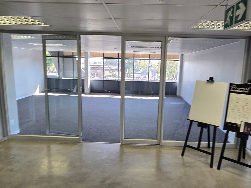 Open plan office space featuring glass partitions, suspended ceilings with recessed lighting, and a combination of carpet and concrete flooring.