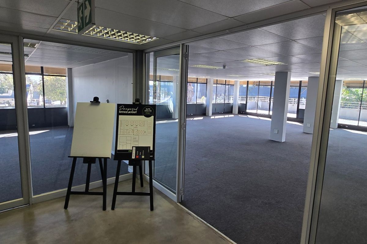 Spacious open-plan commercial office suite featuring glass partitioning, carpeted flooring, and large windows providing ample natural light.