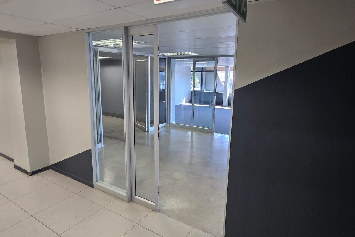 A bright, empty commercial office space featuring glass partitions, modern tiled flooring, and a suspended ceiling with recessed lighting.
