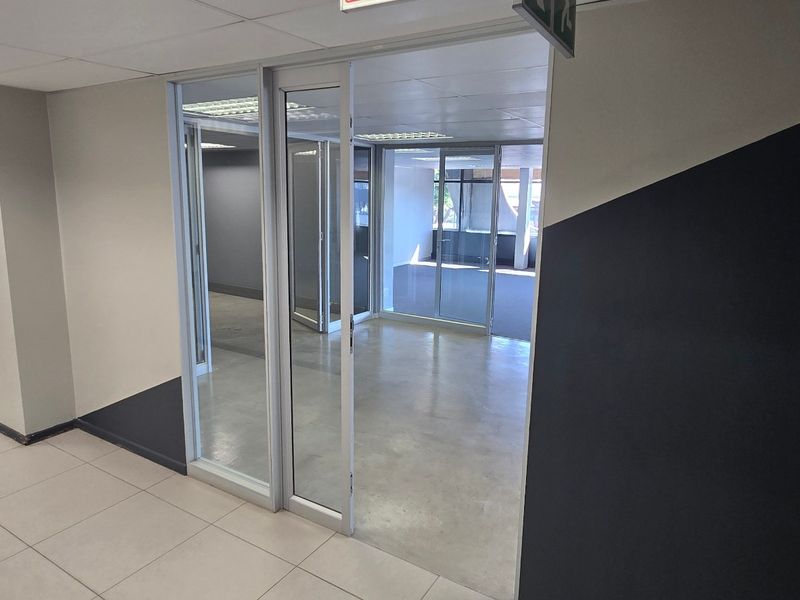 A bright, empty commercial office space featuring glass partitions, modern tiled flooring, and a suspended ceiling with recessed lighting.