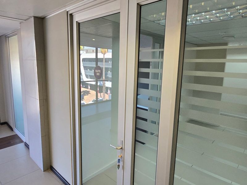 A clean, modern commercial hallway featuring aluminium-framed glass office doors with frosted privacy film, tiled flooring, and recessed ceiling lighting.