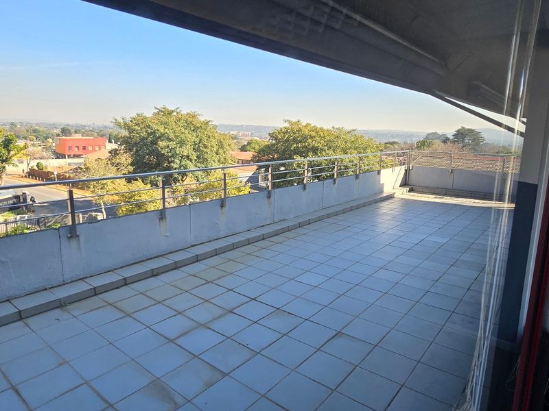 Spacious covered balcony featuring tiled flooring and a stainless steel balustrade, offering an elevated view of the surrounding area.