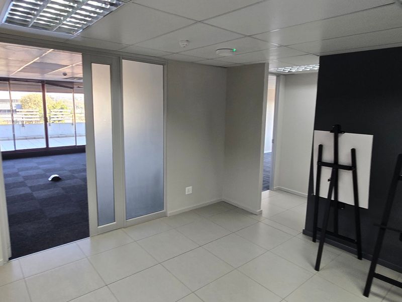 A bright, modern office space featuring tiled flooring, a glass partition door, and a suspended ceiling with recessed lighting.