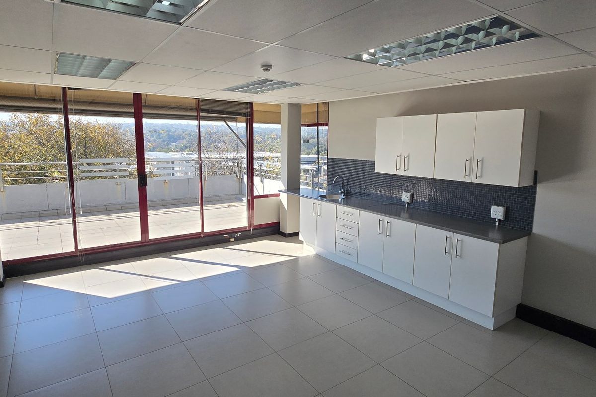 A bright, modern office kitchenette featuring white cabinetry, tiled backsplash, and direct access to a private balcony with scenic views.