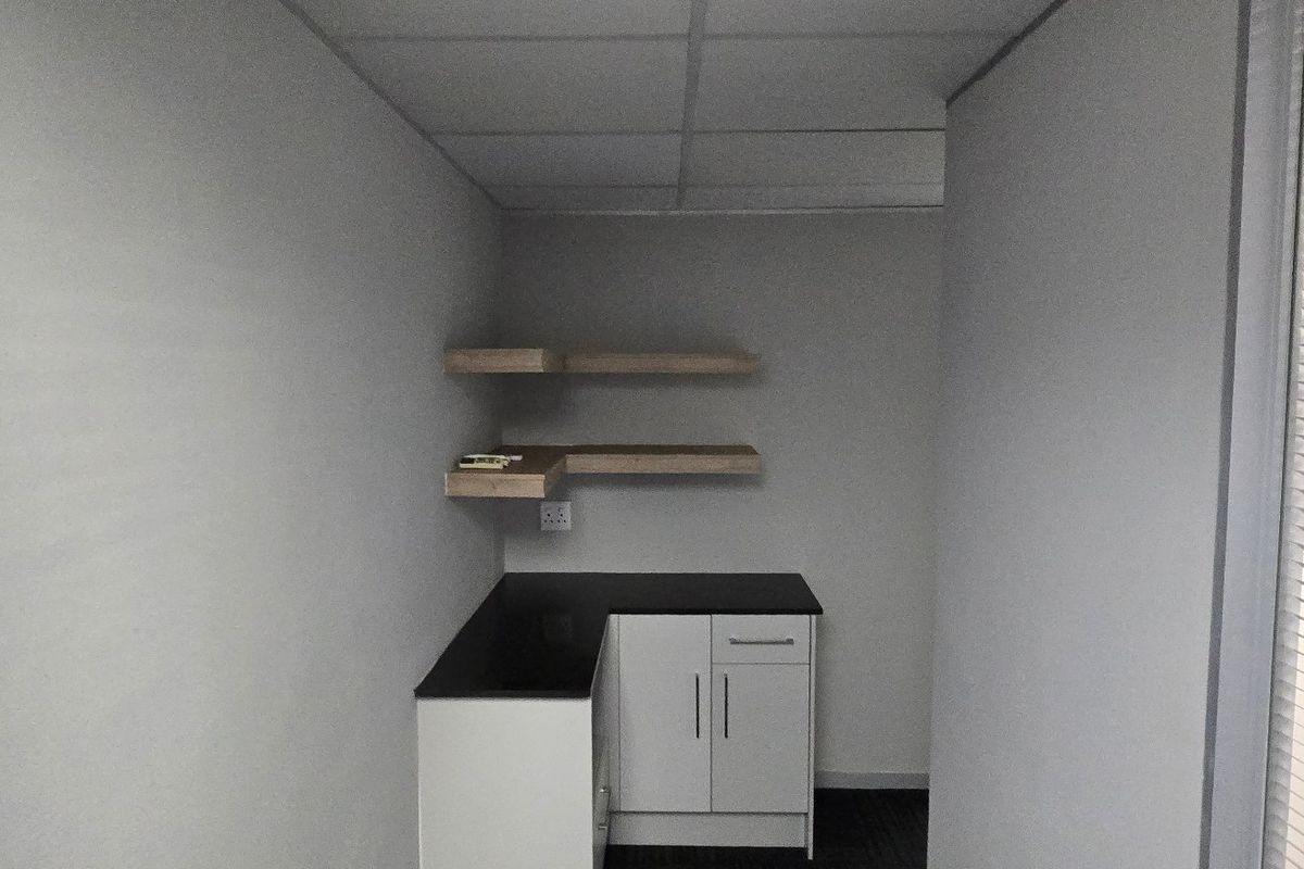 A compact kitchenette area featuring built-in cabinetry, a dark countertop, and floating wall shelves, suitable for a small office or utility space.