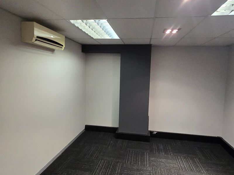 A clean, empty office space featuring carpet tiles, a suspended ceiling with recessed lighting, and a wall-mounted split-system air conditioning unit.
